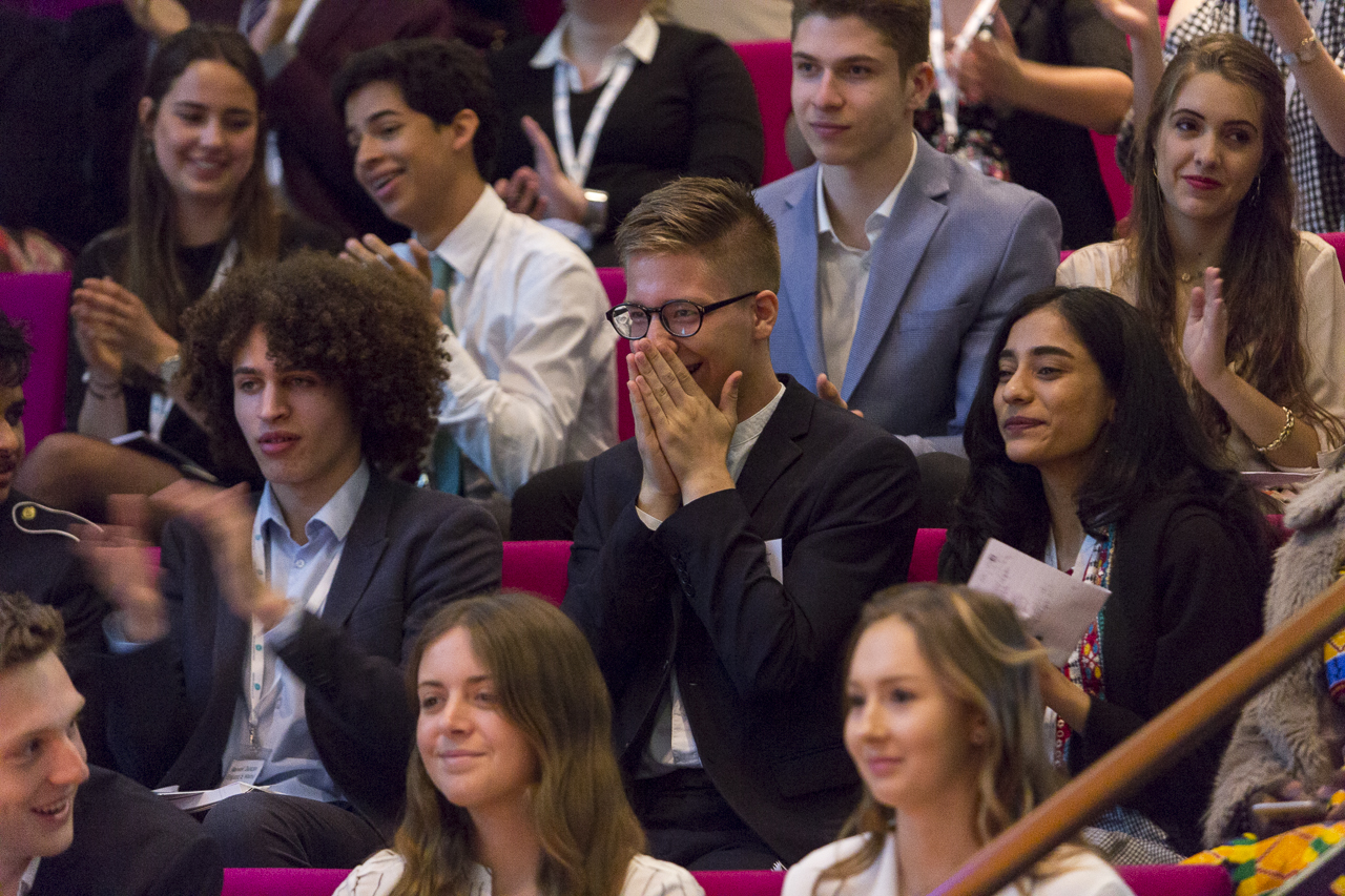 A group of primary and secondary school students (male and female) sitting inside a theatre hall.