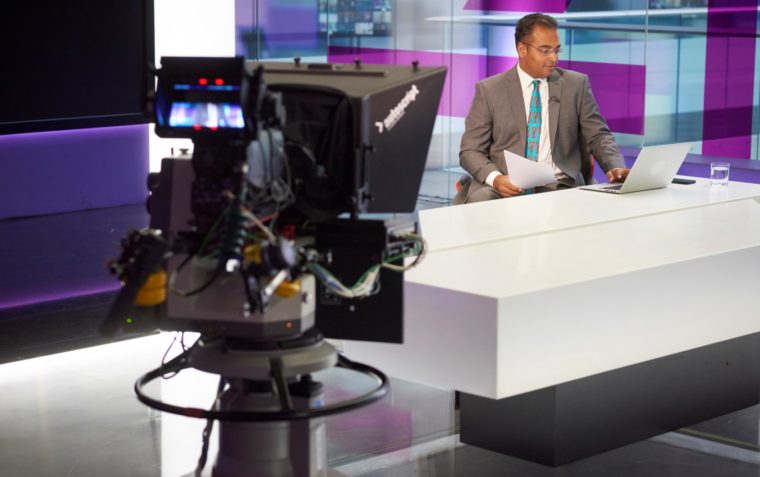 A picture of Krishnan Guru-Murthy sitting inside the studio in front of the camera during a live television broadcast.