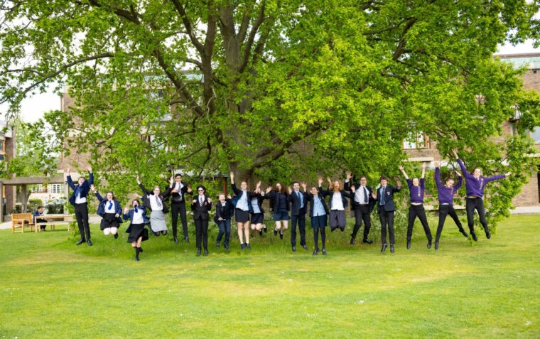 A row of people outside in front of a tree jumping and throwing their arms in the air
